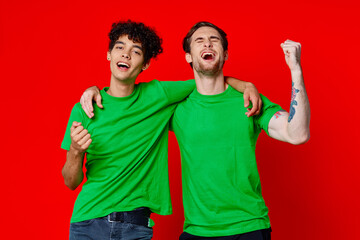 Two cheerful friends hug green t-shirts emotions communication red background