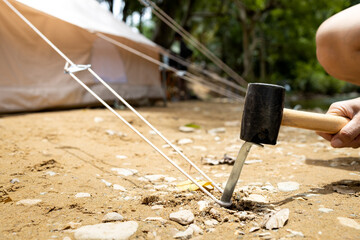 Hand of male holding a rubber mallet,hammering aluminium steel tent stakes pegs nail,fastening tent for camping,hit or beat anchor of the tent into the ground,hammer with rubber head, wooden handle