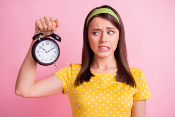 Sticker - Photo of young beautiful unsure uncertain doubtful girl hold and look at clock isolated on pink color background