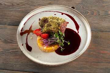 Wall Mural - Top view of beef meat with pistachio topping served with cranberry sauce. Tasty meal with fruits, berries and fresh sprouts presented on ceramic white plate in luxurious restaurant, wooden table.