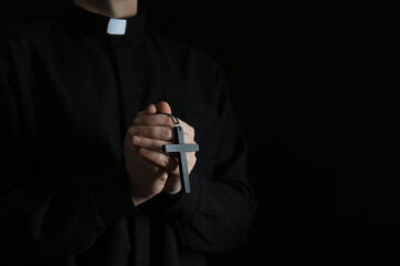 Priest with cross on dark background, closeup. Space for text