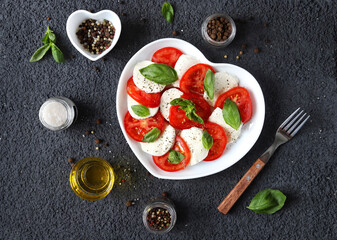 Wall Mural - Caprese salad. Italian salad with fresh tomatoes, mozzarella cheese and basil on a dark background. Top view.