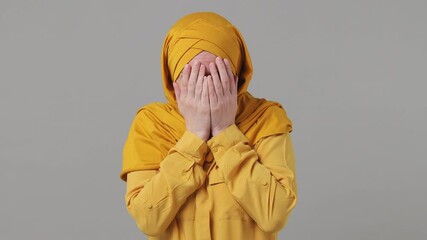 Wall Mural - Scared shocked arabian asian muslim woman in abaya hijab yellow clothes cover hide face with hands peep through fingers isolated grey gray background People uae middle eastern islam religious concept