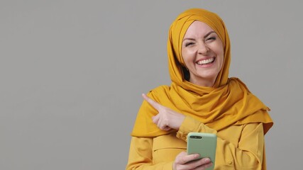 Wall Mural - Arabian asian muslim woman in abaya hijab yellow clothes pointing fingers hands aside on workspace copy space mockup promo area use cellphone isolated on grey gray background People uae islam concept