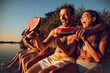 © Zoran Zeremski - Friends sitting on the edge of a pier enjoying on a summer day at the lake eating watermelon.