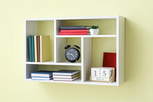Shelf With Books, Alarm Clock And Calendar Hanging On Color Wall