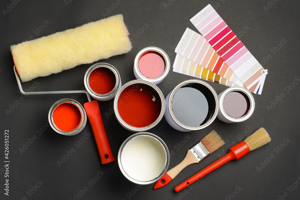 Cans of paints, palette samples, roller and brushes on dark background