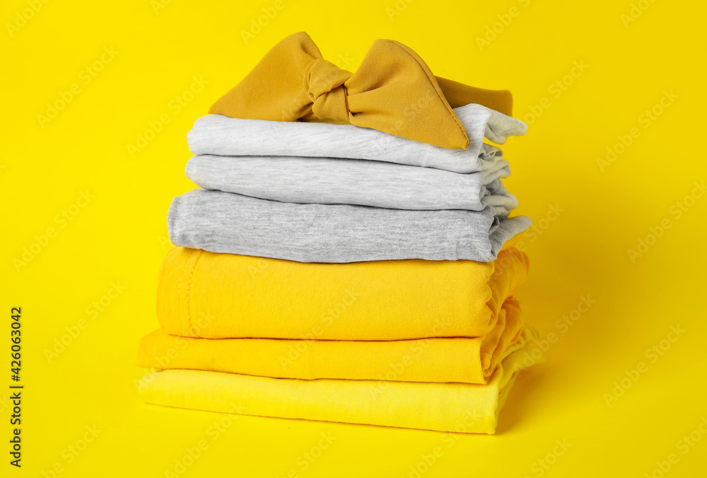 Stack of stylish clothes with hairband on color background