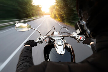 The motorcyclist is riding through the empty asphalt road in the evening