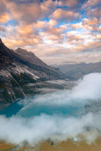 Clouds At Sunset Over The Pristine Lake Oeschinensee In The Mist, Bernese Oberland, Kandersteg, Canton Of Bern, Switzerland