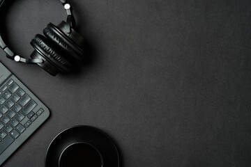 Top view modern office desk with headphones, cup of coffee, laptop computer on black leather background. Flat lay sound producer workspace.