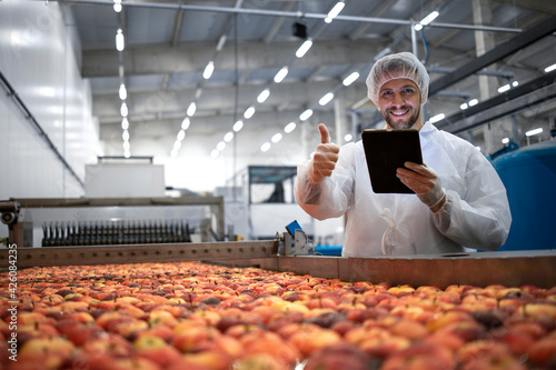 Technologist showing thumbs up in food processing factory and checking quality of apple fruit.