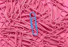 Blue paper clip on pile of pink paper clips
