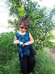 Wall Mural - little child girl playing with flower in hands wearing sunglasses,outdoor green field,