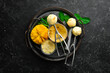 Mango ice cream with mint and fresh mango. Ice cream spoon. On a black stone background, top view.