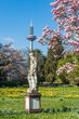 Statue des Pluto vor einem blühenden Magnolienbaum im Palmengarten von Frankfurt und dem Fernsehturm im Hintergrund