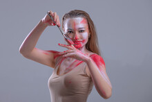 Portrait Of Model Soiled In White And Red Paint Holding Coloring Brush