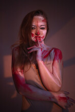 Portrait Of Woman Soiled In White And Red Paint In Soft Light From Window. Grey Background