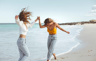 Two women walking together at the beach, hugging each other and smiling