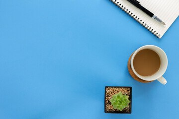 Wall Mural - Top view notebook with coffee cup and cactus isolated on blue background with copy space