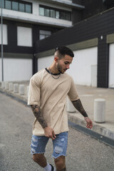 Wall Mural - Young Caucasian male from Spain with tattoos wearing a beige shirt and shorts posing on a street