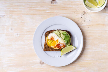 Wall Mural - Poached egg on smashed avocado on brown toast served on white plate