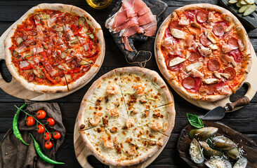 Canvas Print - Variety of meat pizzas with sausage, ham, prosciutto, salami, chicken fillet, pepperoni, shrimps, cheese, greens, vegetables on dark wooden background. Fast food lunch for picnic company, top view