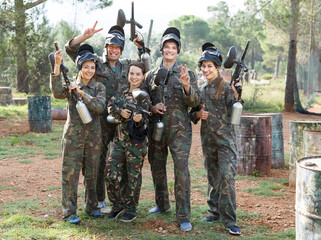 Wall Mural - Happy group of paintball players in camouflage standing with guns on paintball playing field outdoors