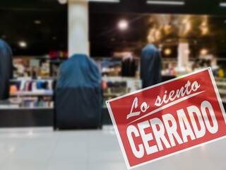 Wall Mural - SORRY WE ARE CLOSED inscription in Spanish. Empty trade mall store with closed red sign due to coronavirus pandemic restrictions