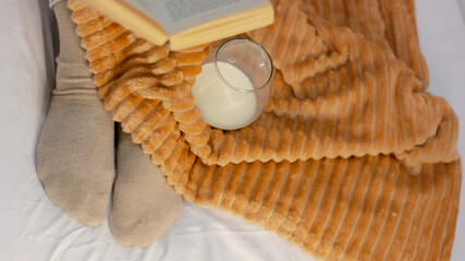 lying feet up on yellow orange shaggy blanket and reading book. Cozy leisure scene, Woman relaxing at home. Comfy lifestyle.