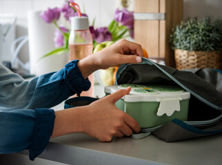 Wall Mural - Schoolboy teenager preparing lunch box putting food container into schoolbag. 