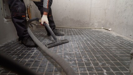 A man vacuums a construction site. Close-up of a cleaner in special clothing holding a brush from an industrial professional vacuum cleaner. A worker vacuums the bathroom floor before laying.