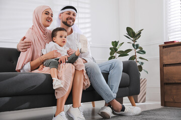 Wall Mural - Happy Muslim family spending time together on sofa at home, space for text