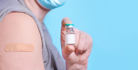 man with a bottle of vaccine and a plaster on his shoulder after getting covid-19 vaccine on a blue 