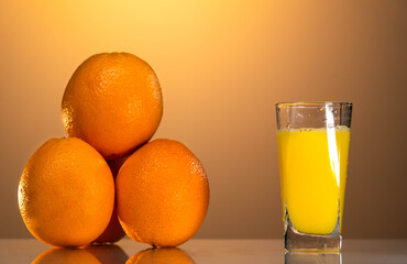 a glass of organic fresh orange juice and some oranges on the reflection table with the sunset background