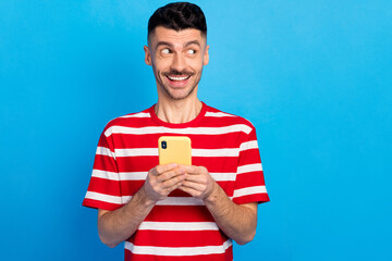 Sticker - Photo of dreamy creative young man look empty space imagine post hold phone isolated on blue color background