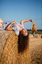 Attractive Woman Posing In The Mown Wheat Fields With Sheaf And Sky In The Village. Hay Bales In The Field After Harvest