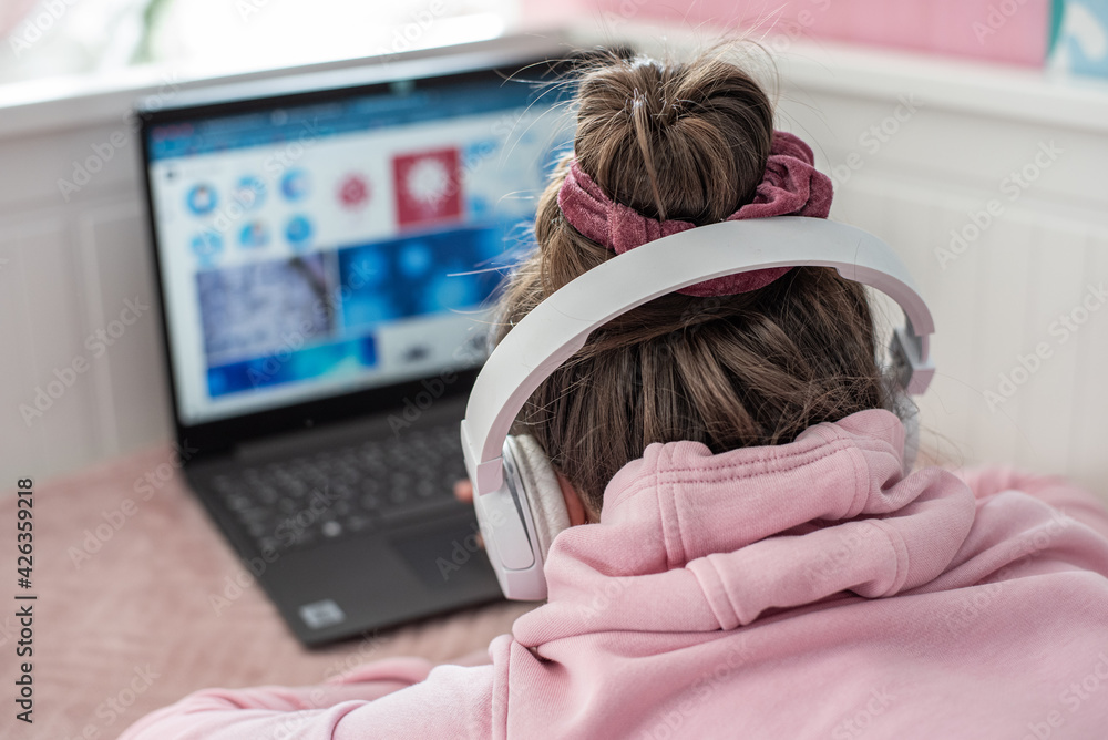 Nauka zdalna w domu . Dziewczynka pracuje na komputerze ze słuchawkami na uszach. - obrazy, fototapety, plakaty 