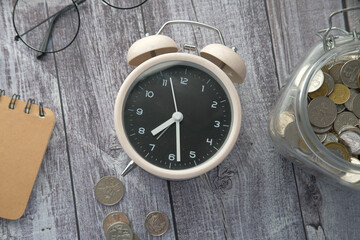 old alarm clock , notepad and coins on wooden table 