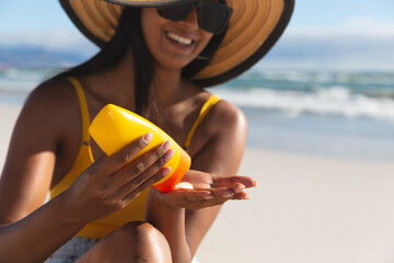 Wall Mural - Smiling mixed race woman on beach holiday using sunscreen cream