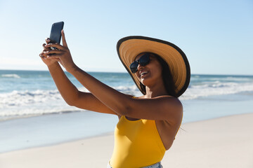 Wall Mural - Smiling mixed race woman on beach holiday taking selfie