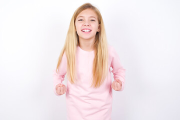 Wall Mural - beautiful caucasian little girl wearing pink hoodie over white background raising fists up screaming with joy being happy to achieve goals.