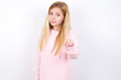 No sign gesture. Closeup portrait unhappy beautiful caucasian little girl wearing pink hoodie over white background raising fore finger up saying no. Negative emotions facial expressions, feelings.