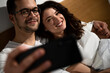 © Zoran Zeremski - Smiling couple in the morning laying in bed in the bedroom making selfie.