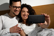 © Zoran Zeremski - Smiling couple in the morning laying in bed in the bedroom making selfie.