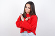 © Jihan - young beautiful brunette woman wearing red knitted sweater over white wall Has rejection angry expression on face and crossing hands doing refusal negative sign.