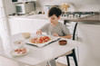 © Olga Krivokoneva - Little kid boy making pizza sitting at the table on the kitchen. Children helping in cooking lifestyle image
