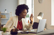 © Studio Romantic - Friendly african american businesswoman holds an online meeting while sitting in the office. Woman waving hand greeting participants of a video call. Online business concept.