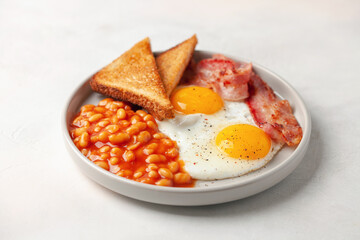 Continental breakfast - eggs, toast, bacon and beans in tomato sauce on a plate on the table.