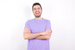 © Jihan - young handsome caucasian man wearing purple t-shirt against white background being happy smiling and crossed arms looking confident at the camera. Positive and confident person.